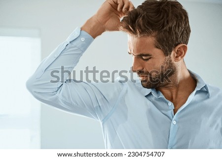 Shirt, stress with man smelling armpit sweat stain and indoors at his home. Hygiene or hyperhidrosis, deodorant protection for sweaty mark on clothing and young male person sweating with wet spot Royalty-Free Stock Photo #2304754707