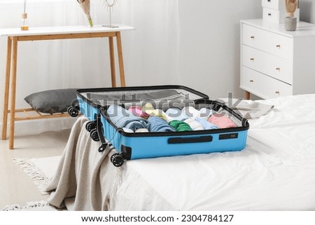Open suitcase with folded clothes on bed in room Royalty-Free Stock Photo #2304784127