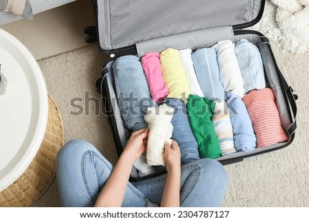 Woman packing clothes into suitcase on floor at home, closeup Royalty-Free Stock Photo #2304787127