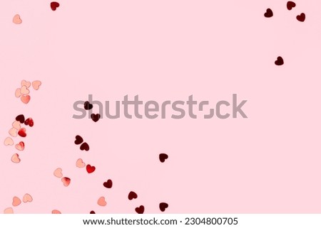 Metallic red confetti in a heart shape scattered on a pink background. Composition with copy space.