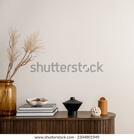 Minimalist composition of living room interior with copy space, wooden commode, vase with dried flowers, candle, black books and personal accessories. Home decor. Template.  Royalty-Free Stock Photo #2304801949