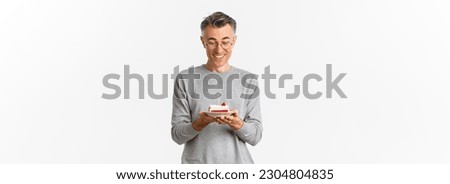 Image of happy, attractive middle-aged man in glasses and grey sweater, celebrating his birthday, smiling and looking at b-day cake, making a wish, standing over white background.