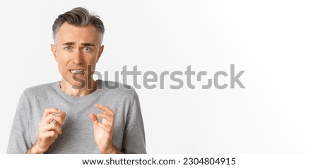 Close-up of anxious middle-aged man, looking scared and nervous, feeling guilty, standing over white background. Royalty-Free Stock Photo #2304804915