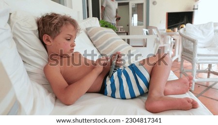 Child lying on sofa playing video-game on smartphone device, casual and candid