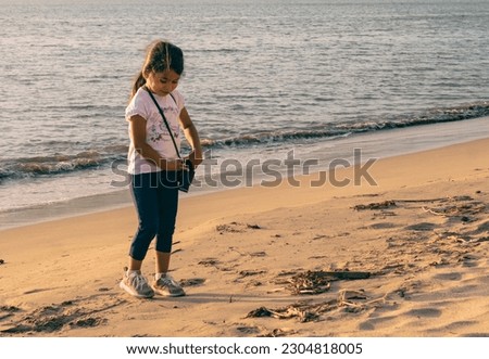 Girl Looking at the beach through binoculars on a sunny afternoon, backlit, walking and smiling, kicking up the sand. looking to the camera