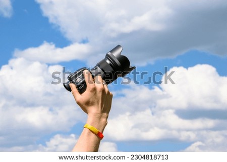Hand holding a photo camera on a blue sky background.  Clouds coming out of the camera