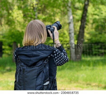 Woman with blonde hair with a backpack on her back photographing an object in the forest, summer and photographer