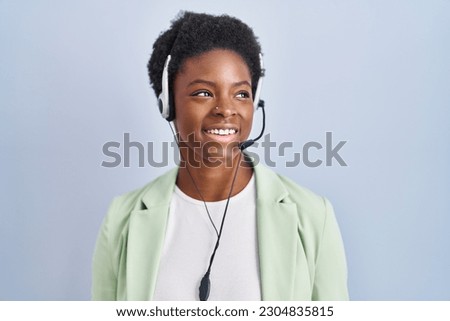African american woman wearing call center agent headset looking away to side with smile on face, natural expression. laughing confident.  Royalty-Free Stock Photo #2304835815