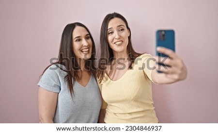 Two women smiling confident make selfie by smartphone over isolated pink background
