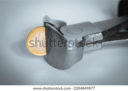 A pincer bites into a coin worth one euro, concept of rising inflation. Royalty-Free Stock Photo #2304849877