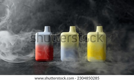 A set of multicolored disposable electronic cigarettes on a dark background stand on a table with smoke around. The concept of modern smoking, vaping and nicotine Royalty-Free Stock Photo #2304850285
