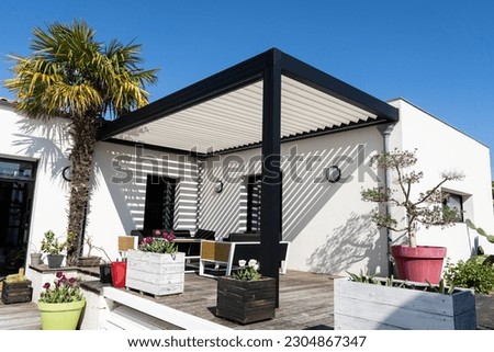 eco friendly bioclimatic aluminum pergola shade structure, awning and patio roof, garden lounge, chairs, metal grill surrounded by landscaping Royalty-Free Stock Photo #2304867347