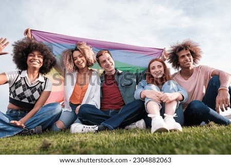 Group of young people sitting on the grass with the gay pride flag. Concept: friendship, lgtbi, symbols.