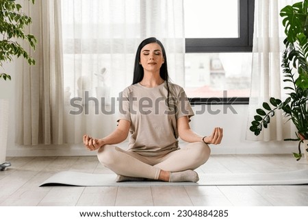 Young woman meditating sitting on a yoga mat near a big window Royalty-Free Stock Photo #2304884285