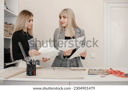 Two young dressmakers standing in the atelier while making a sketch