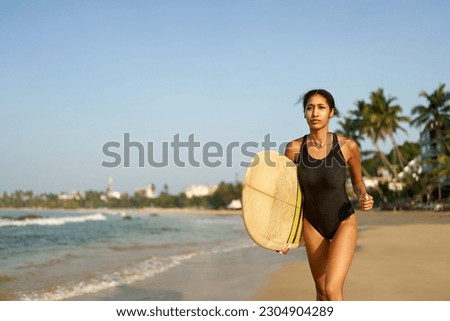 African american woman running with surfboard on ocean beach. Black female surfer with surf board. Pretty multiethnic girl goes on surfing session on tropical location at sunny sunrise.