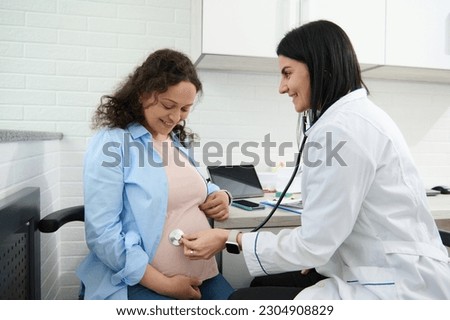 Confident female doctor obstetrician gynecologist checking heartbeat of the baby in womb using a stethoscope, examining a pregnant woman in gynecological clinic. Gynecology consultation. Pregnancy Royalty-Free Stock Photo #2304908829