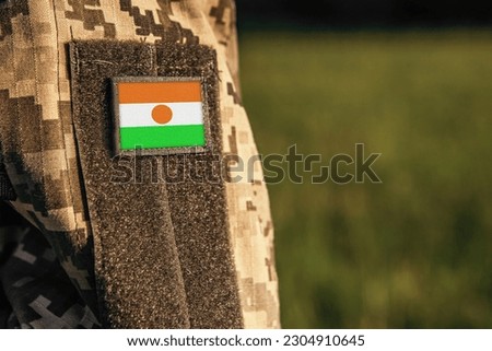 Close up millitary woman or man shoulder arm sleeve with Niger flag patch. Troops army, soldier camouflage uniform. Armed Forces, empty copy space for text

