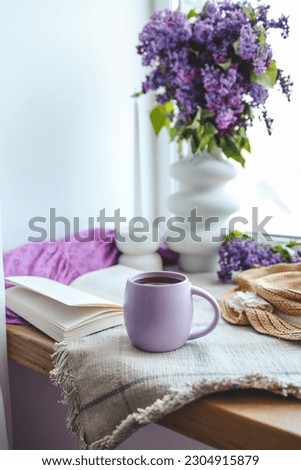 Cup of tea, straw hat, open book and lilac basket, spring still life.