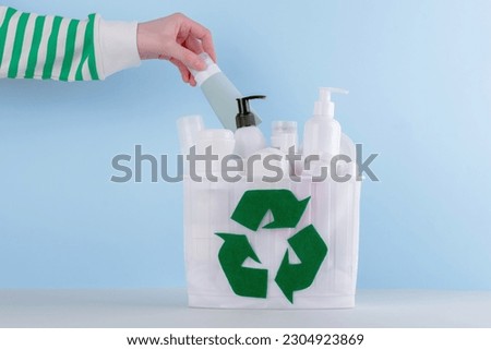 Female's hand putting used cream in the bin with green recycling symbol on blue background. HDPE. Plastic garbage. Sorting and recycling of cosmetic products. Save the planet. High quality photo