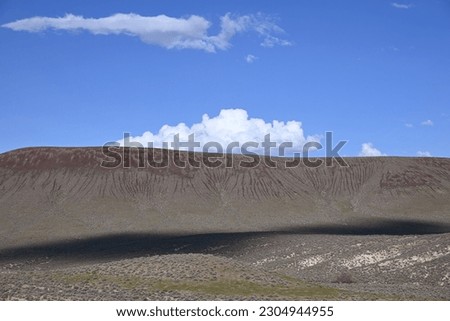 White clouds on top of top of flat mountain with shadow on base of hill.