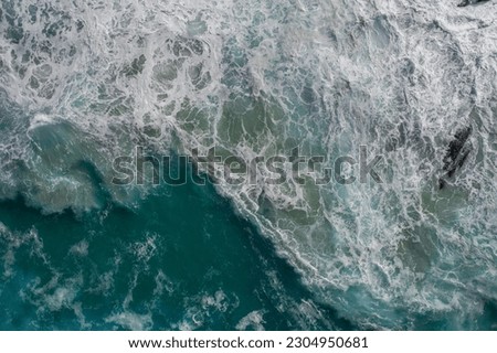 Aerial view of a strong wave crashing with surfers nearby 