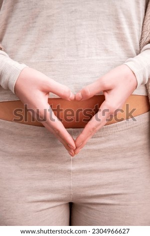 Closeup on young woman holding hands in heart shape on her belly