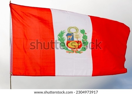 Large flag of Peru fixed on metal stick waving against background of cloudy sky during daytime