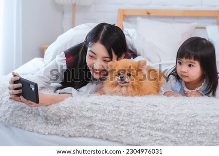After taking the picture the asian girl showed it to the little girl and they both admired how cute they all looked together on the bed with the furry friend.