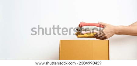 Donation, Charity, Volunteer, Giving, Delivery and Home Moving Concept. Hand holding Clothes into cardboard box at home for support and help poor, refugee and homeless people. Copy space for text Royalty-Free Stock Photo #2304990459