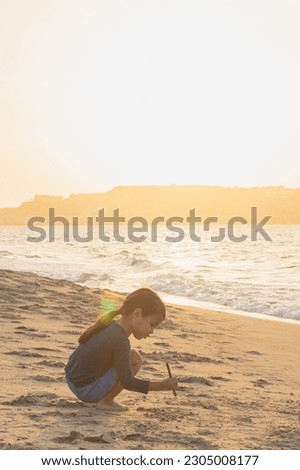 girl playing with the sand of Playa los canals in Lechería, during a golden sunset, Little girl on beach sand, barefoot playing with the sand, sunset in the background.