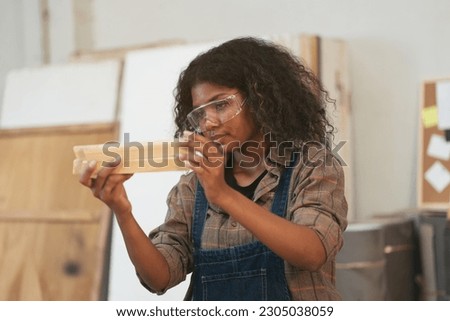 Female carpenter working in wood workshop. Female joiner wearing safety uniform and working in furniture workshop Royalty-Free Stock Photo #2305038059