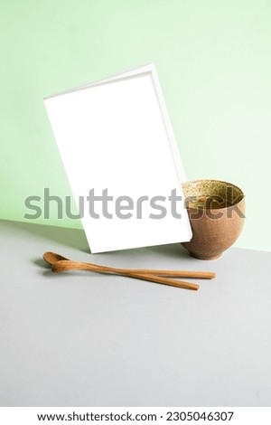 Book cover mockup with cup of tea and wooden spoon on green and gray background. Japanese concept.