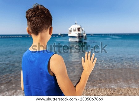 Little boy on the beach with a tourist boat in the background