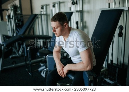 The Aftermath of Dedication A male gym goer finds tranquility and rest after a challenging training session. A tired guy seeks relaxation and relief from fatigue after a demanding workout at the gym. Royalty-Free Stock Photo #2305097723