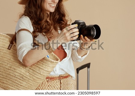 Beach vacation. happy elegant woman in white blouse and shorts isolated on beige background with straw bag, trolley bag and photo camera.