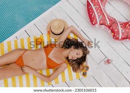 Blissful slim girl in orange swimsuit with relax emotions lying near the pool enjoying summer weekend under warm sun. joyful young woman in beach outfit having fun spending time on exotic resort