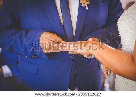 This beautiful image captures the intimate moment of a couple exchanging wedding rings at a real wedding. The photograph features a close-up of the couple's hands, showcasing their intertwined fingers