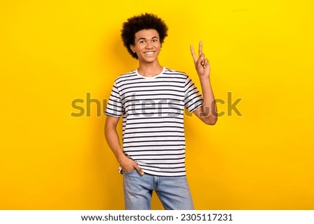 Photo of young friendly guy wear striped t-shirt show v-sign fingers peace symbol model fashion brand isolated on yellow color background