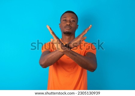 young man wearing orange T-shirt over blue studio background Rejection expression crossing arms doing negative sign, angry face
