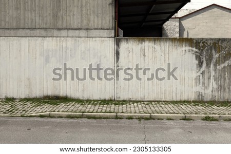 Grunge concrete wall at the roadiside with tiled cement sidewalk overgrown with weeds. Background for copy space.