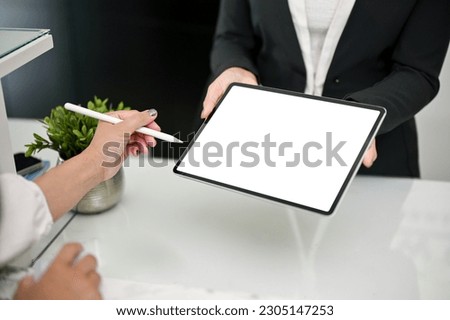 Close-up image of a female receptionist is handing a digital tablet to a customer to sign at the front desk. Tablet white screen mockup, Hotel check-in, Hospitality service concept