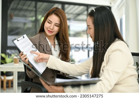 Attractive millennial Asian businesswoman focuses on listening to her colleague give advice for her work on the report, discussing work and working in the office together.