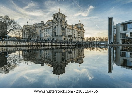 historic Reichstag building in Berlin during the day in winter. River Spree with reflection from the building in the government district. Sunshine in the background with cloudy skies. Royalty-Free Stock Photo #2305164755