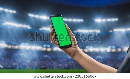 Sport Stadium Championship: Person's Hand Holding Green-Screen Chroma Key Smartphone. Sports Event with Fans Cheering for Favourite Team to Win Championship. Isolated POV Close-up Copyspace Template