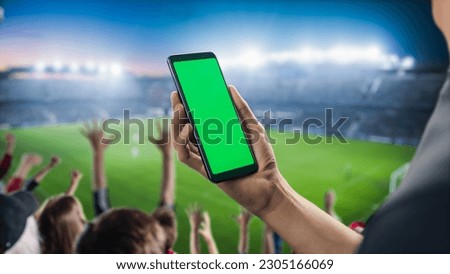 Sport Stadium Championship: Person's Hand Holding Green-Screen Chroma Key Smartphone. Sports Match with Fans on Tribune Cheering for Favourite Team to Win. Isolated POV Close-up Copyspace Template. Royalty-Free Stock Photo #2305166069