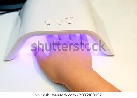 Woman's hand in an electric nail dryer with UV light. Thorough and healthy nail care Royalty-Free Stock Photo #2305183237