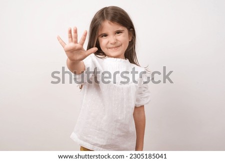 Cute charming little girl wearing white shirt over white background pointing up with fingers number five or making stop gesture. Girl making high five 