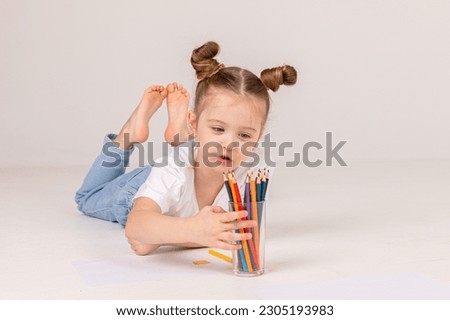 A little girl draws with colored pencils on the floor. High quality