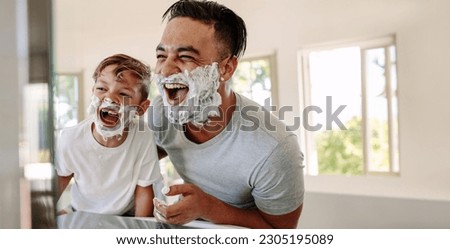 Father and son having fun in a bathroom, laughing happily with shaving foam on their faces. Young single dad taking a moment to bond and share moments of joy with his boy on father's day. Royalty-Free Stock Photo #2305195089